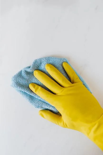 Individual in protective gear cleaning microwave using spray bottle and cloth indoors.